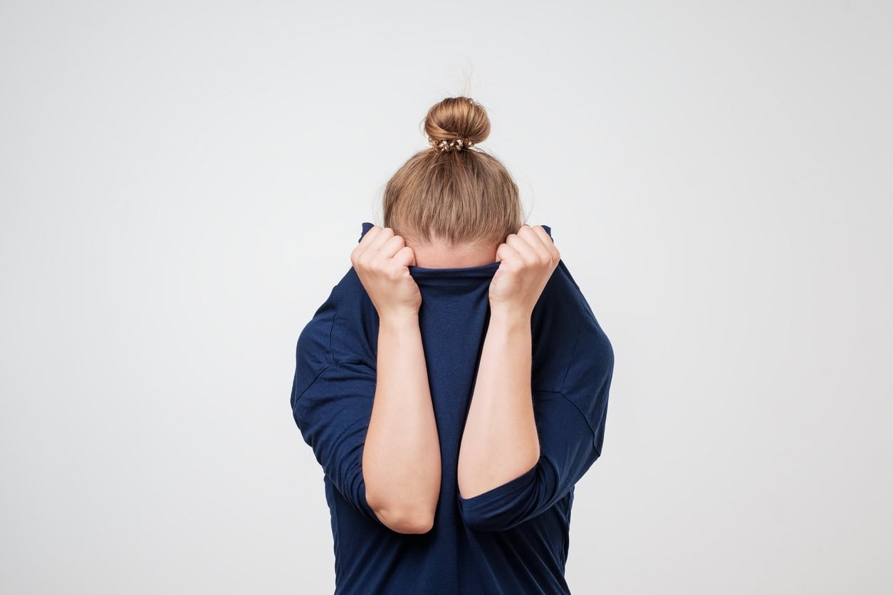 A person with a bun hairstyle hiding their face while pulling a navy blue shirt over their head